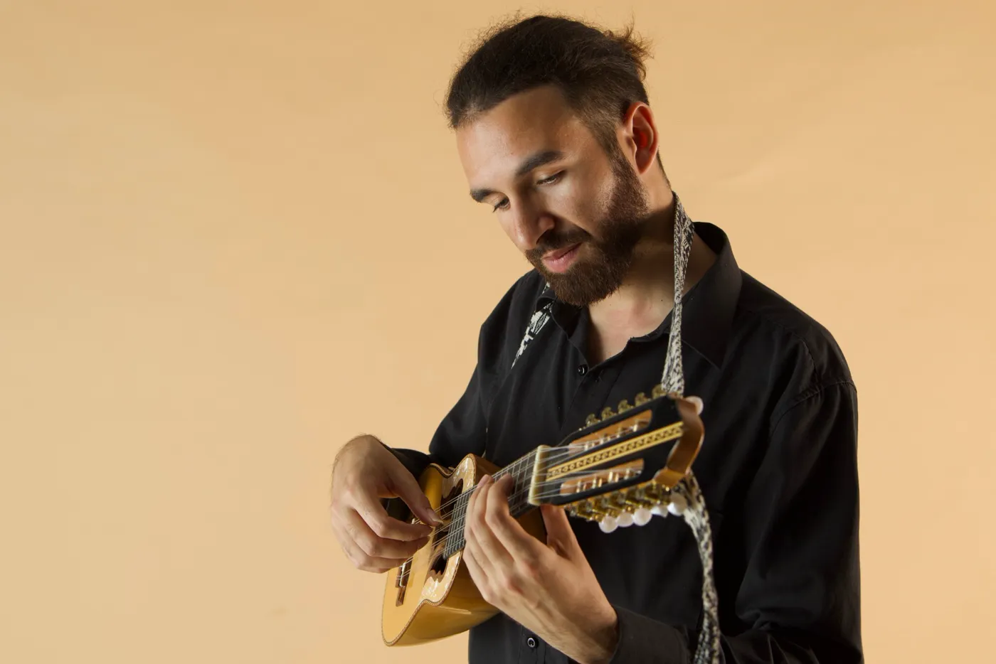 Bruno Meschi smiles as he plays a charango with a light-coloured top