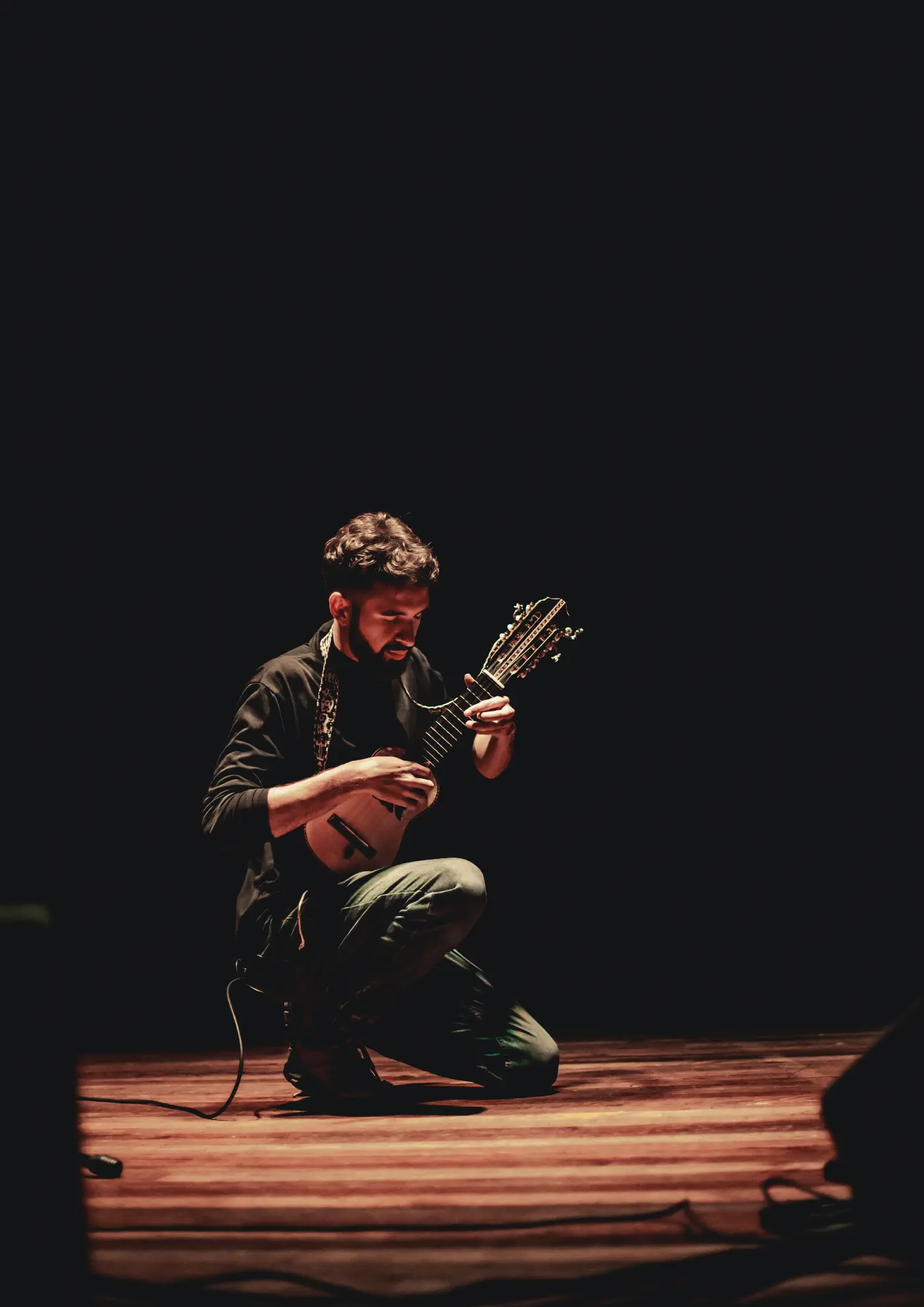 Bruno Meschi kneels on stage, playing the charango under a warm spotlight