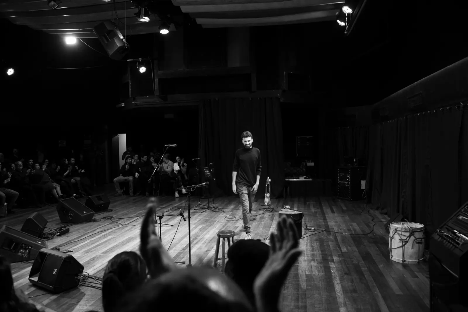 In black and white, Bruno Meschi walks across the stage as the audience applauds
