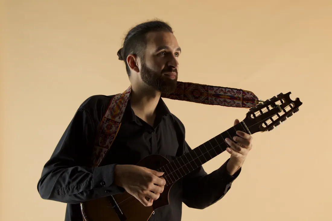 Bruno Meschi plays the charango and looks to one side; the woven strap flies towards the headstock